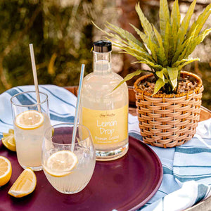 Newy Distillery Lemon Drop Pre-Mix Cocktail. Displayed on purple tray with lime and lemon wedges. Two cocktail drinks in the foreground.