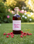 Bottle of Raspberry Vodka on grass with raspberries around, blurred garden background