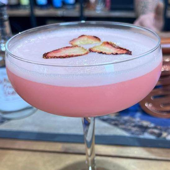 Pink cocktail with strawberry slices in a glass on a wooden surface