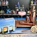 A Strawberry Cheesecake Cocktail Kit presented on a table, including bottles of alcohol and a cocktail shaker, with a box that has 'Cocktail Kit' written on it.